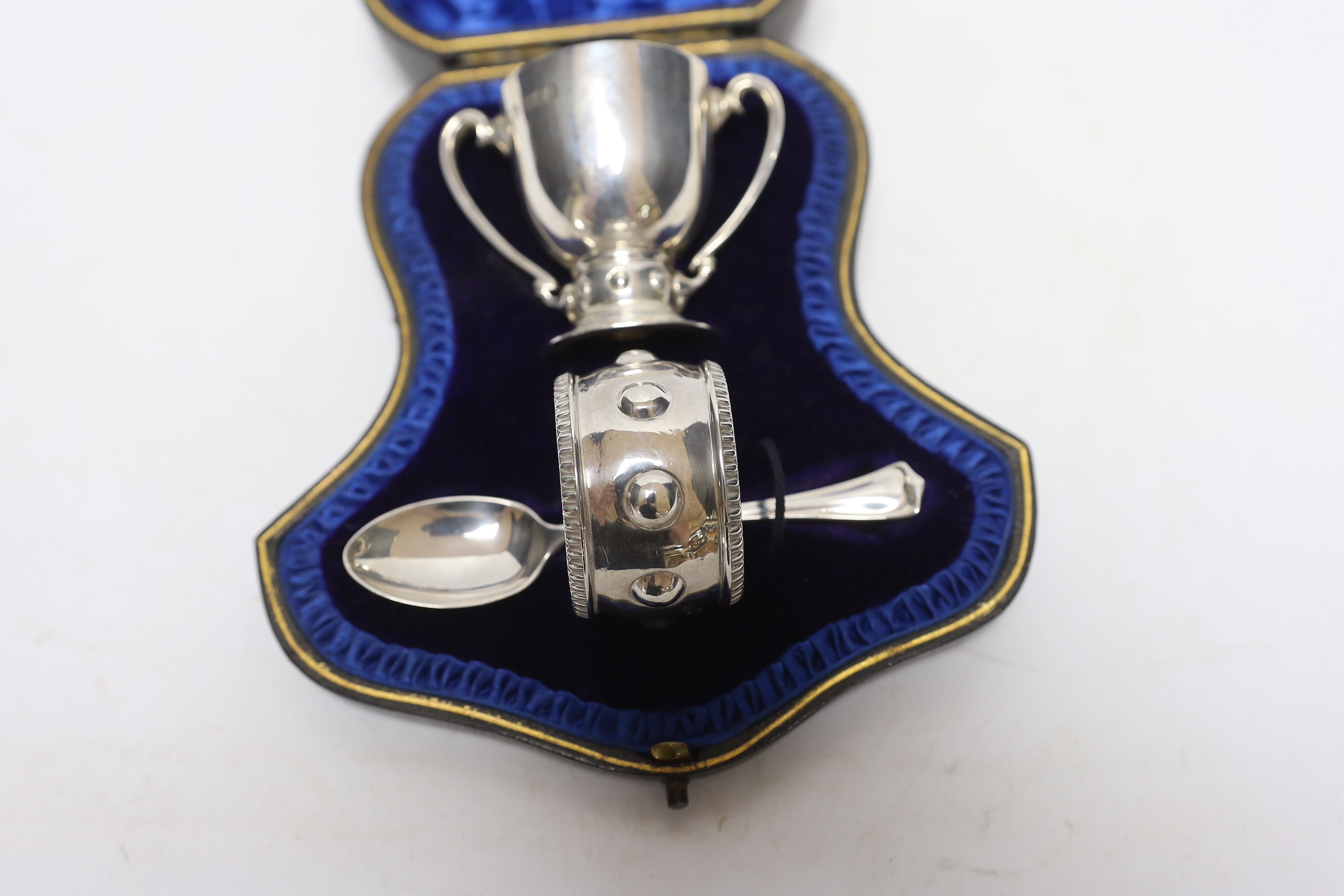 A cased Edwardian matched silver christening pair, (egg cup and napkin ring), Wakeley & Wheeler, London, 1905/6, with associated silver spoon.